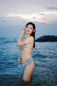 Smiling woman in a bikini enjoying the ocean at twilight with a serene beach backdrop.