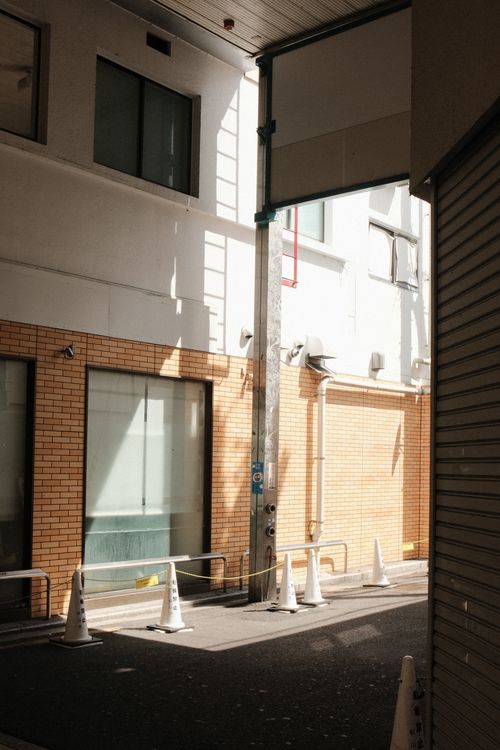 Free A sunlit urban alleyway with traffic cones casting shadows against brick walls, creating a dramatic contrast. Stock Photo