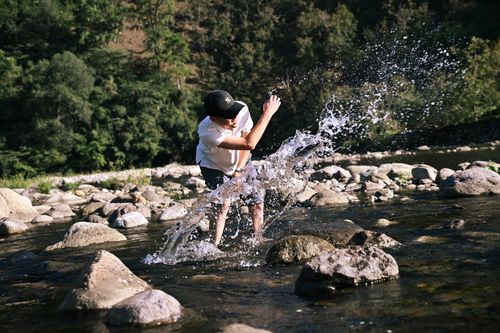 Free A man splashes water in a rocky river setting, capturing the joy of a sunny outdoor experience. Stock Photo