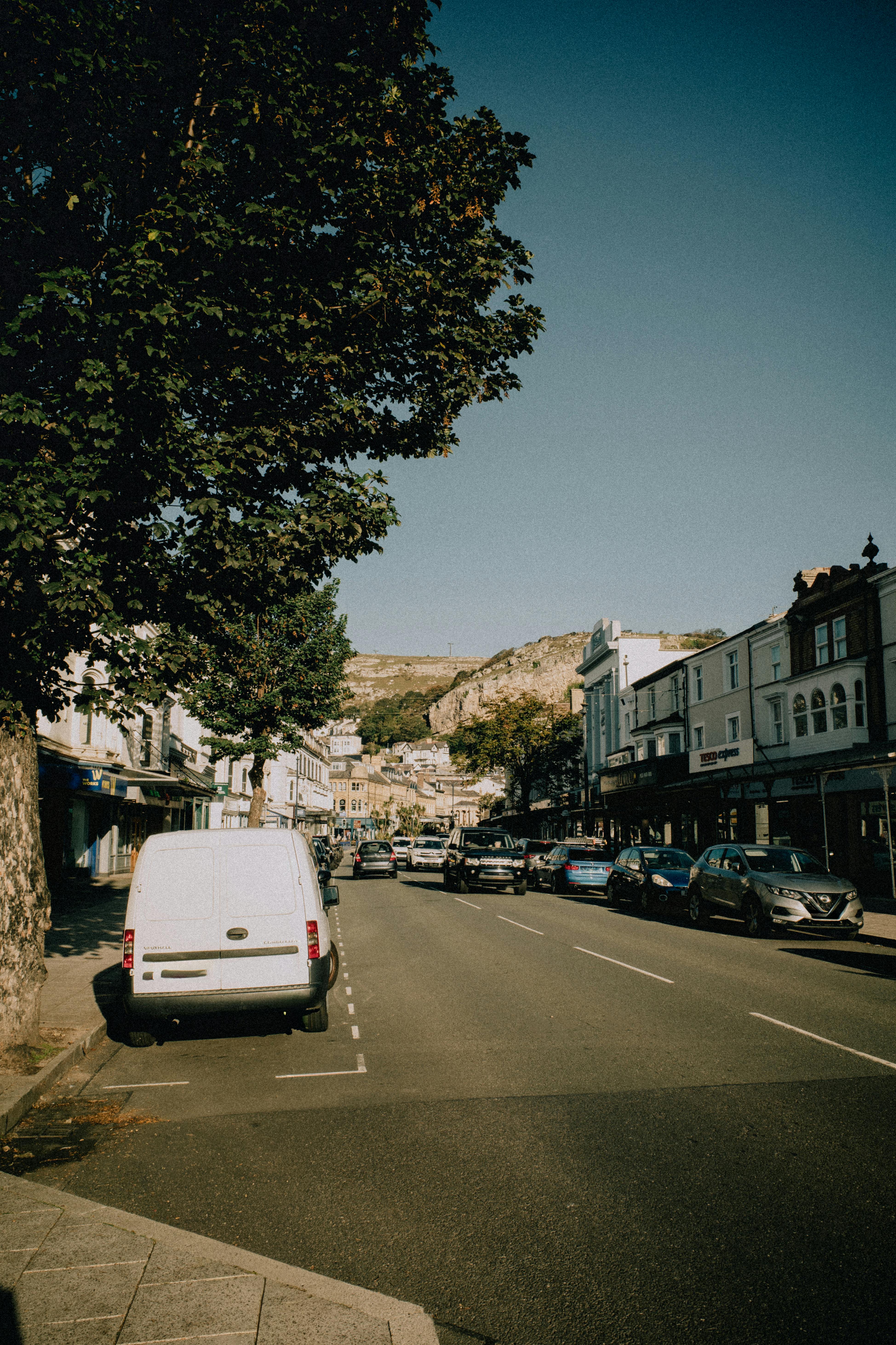 Charming street view of Llandudno with vehicles and historic buildings under a clear sky.