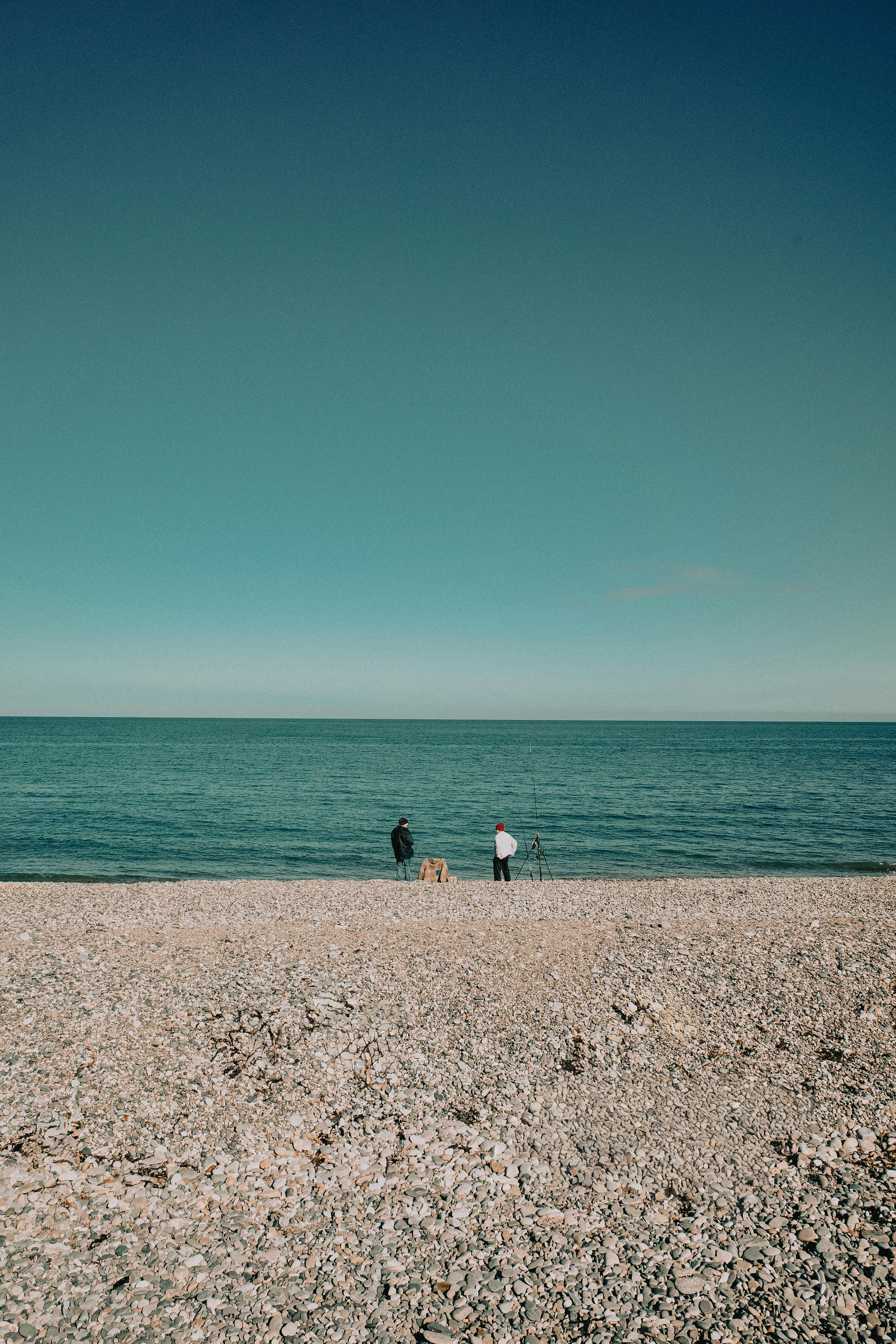 A peaceful beach scene in Llandudno, Wales with two people by the sea under a clear blue sky.