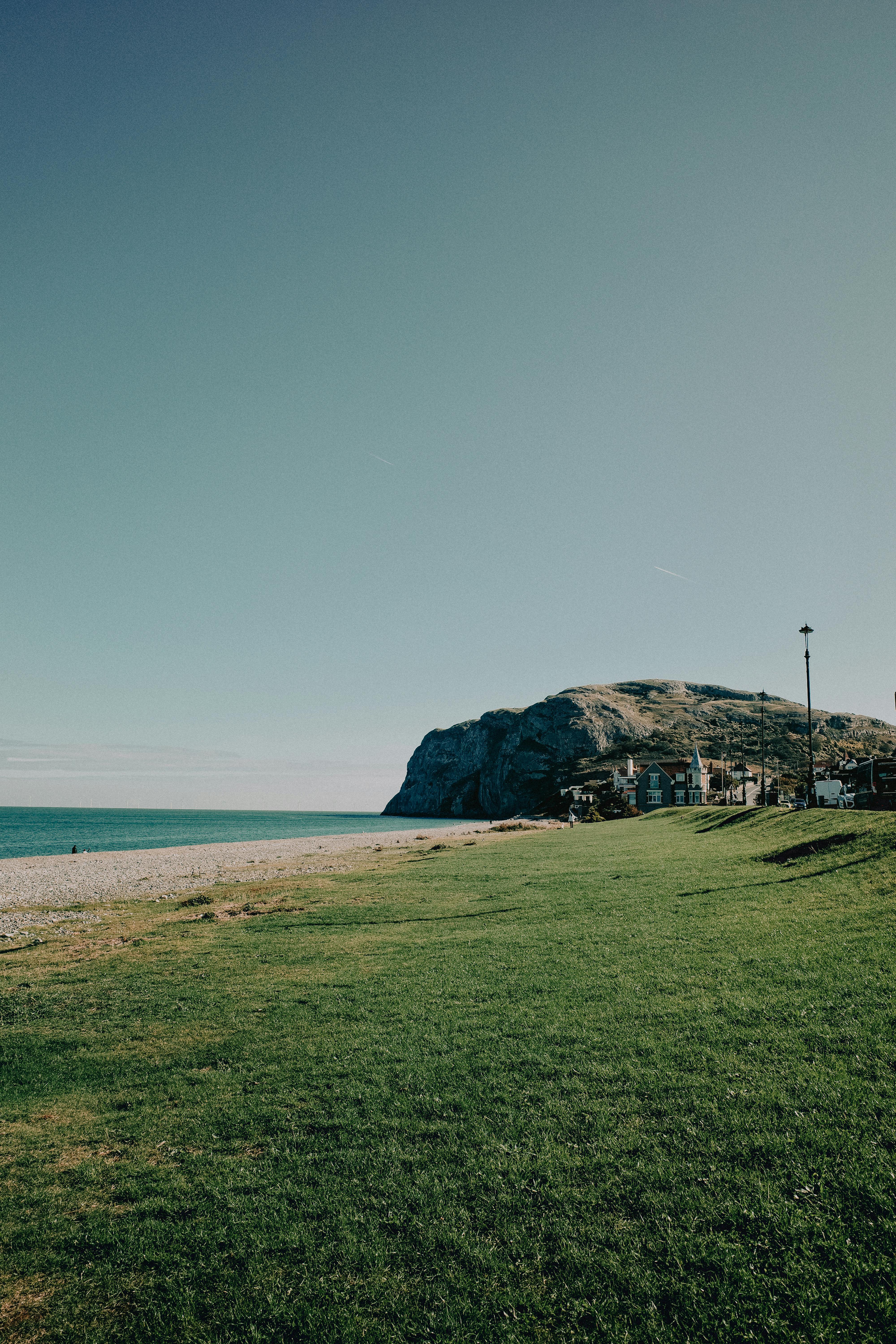 Scenic view of Llandudno's Great Orme with a peaceful beach and grassy foreground under a clear sky.
