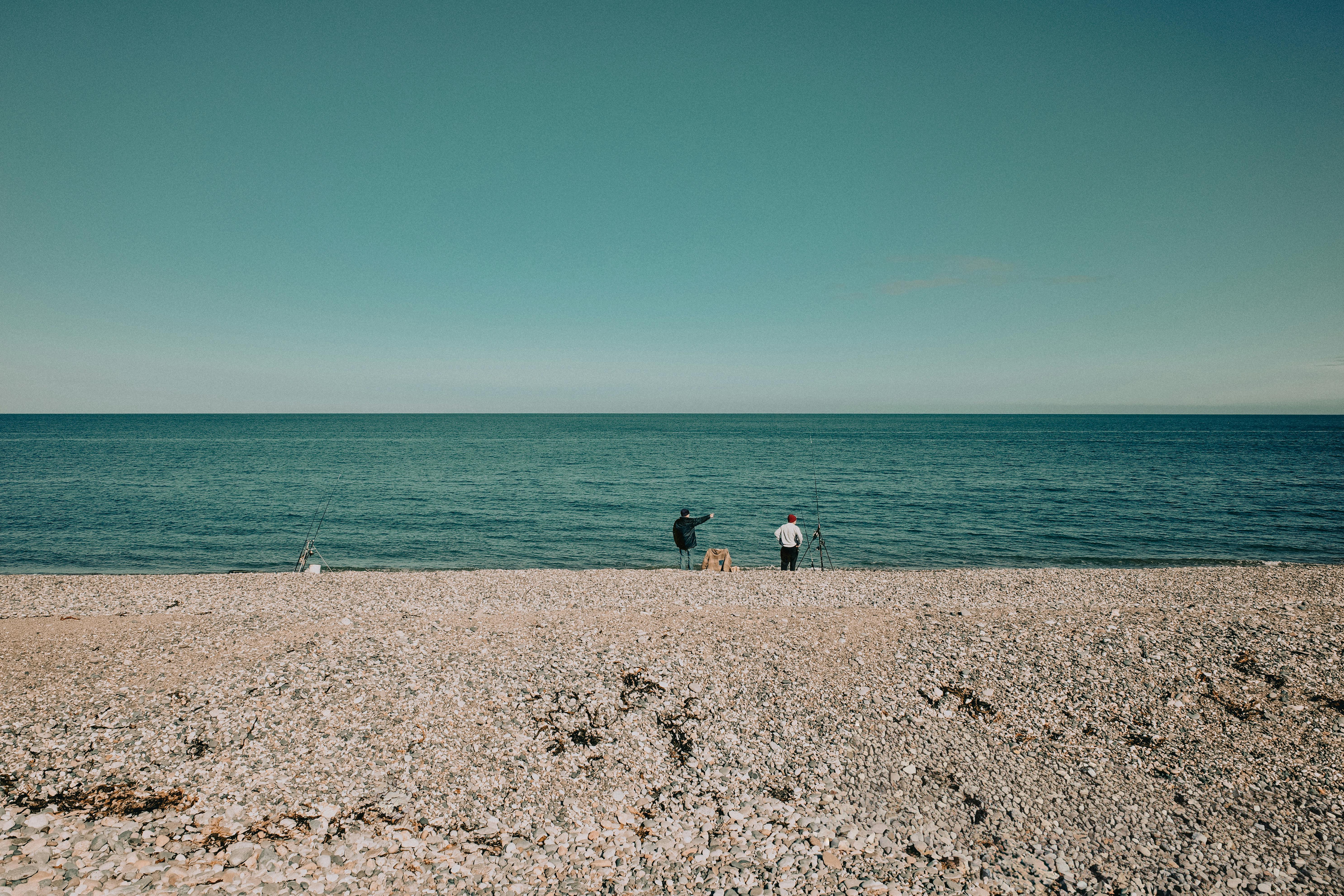 Two people fishing on a pebble beach in Llandudno, Wales on a clear summer day.