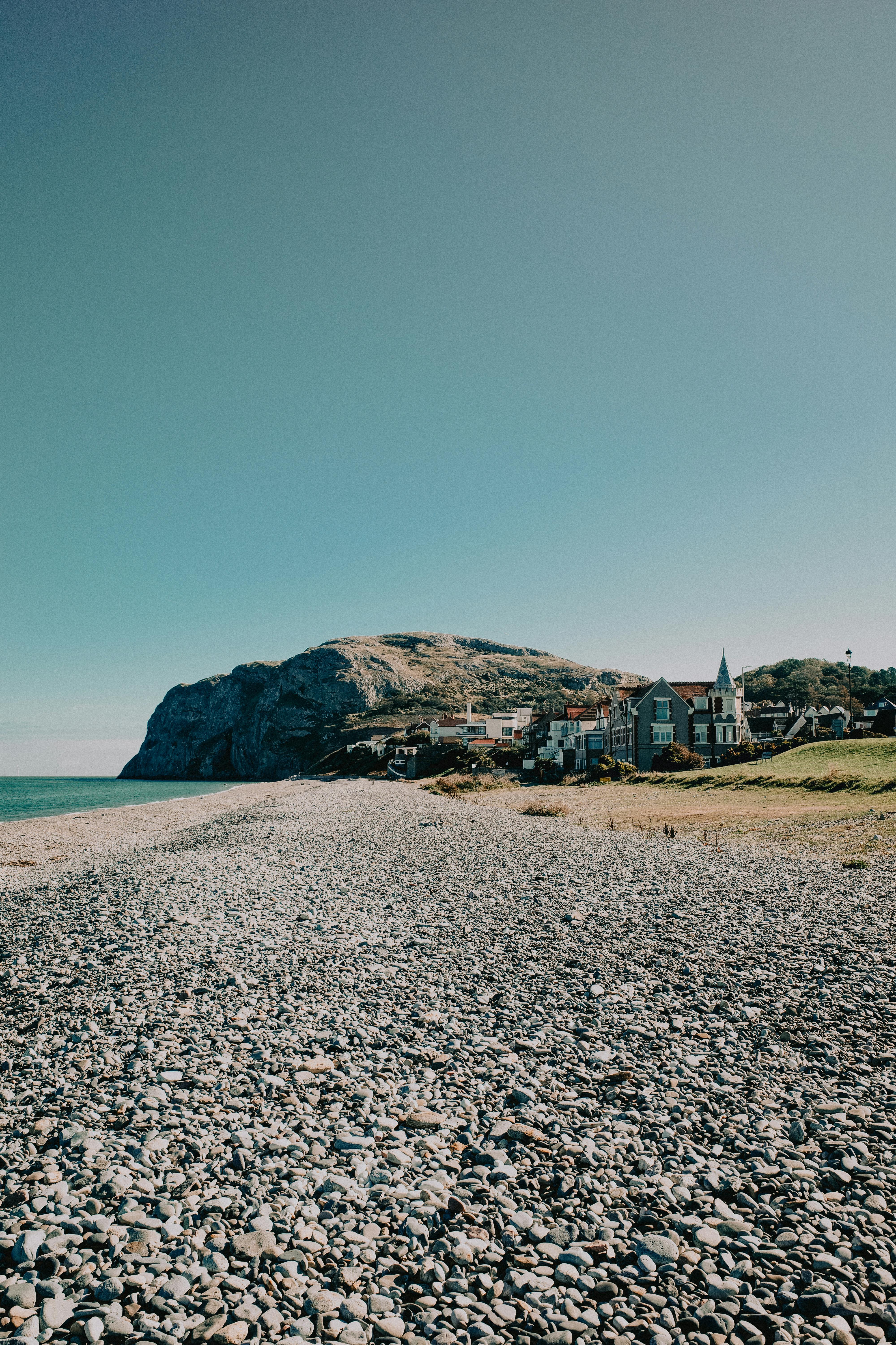 A tranquil view of a pebble beach and coastal houses near Llandudno, Wales, under a clear sky.