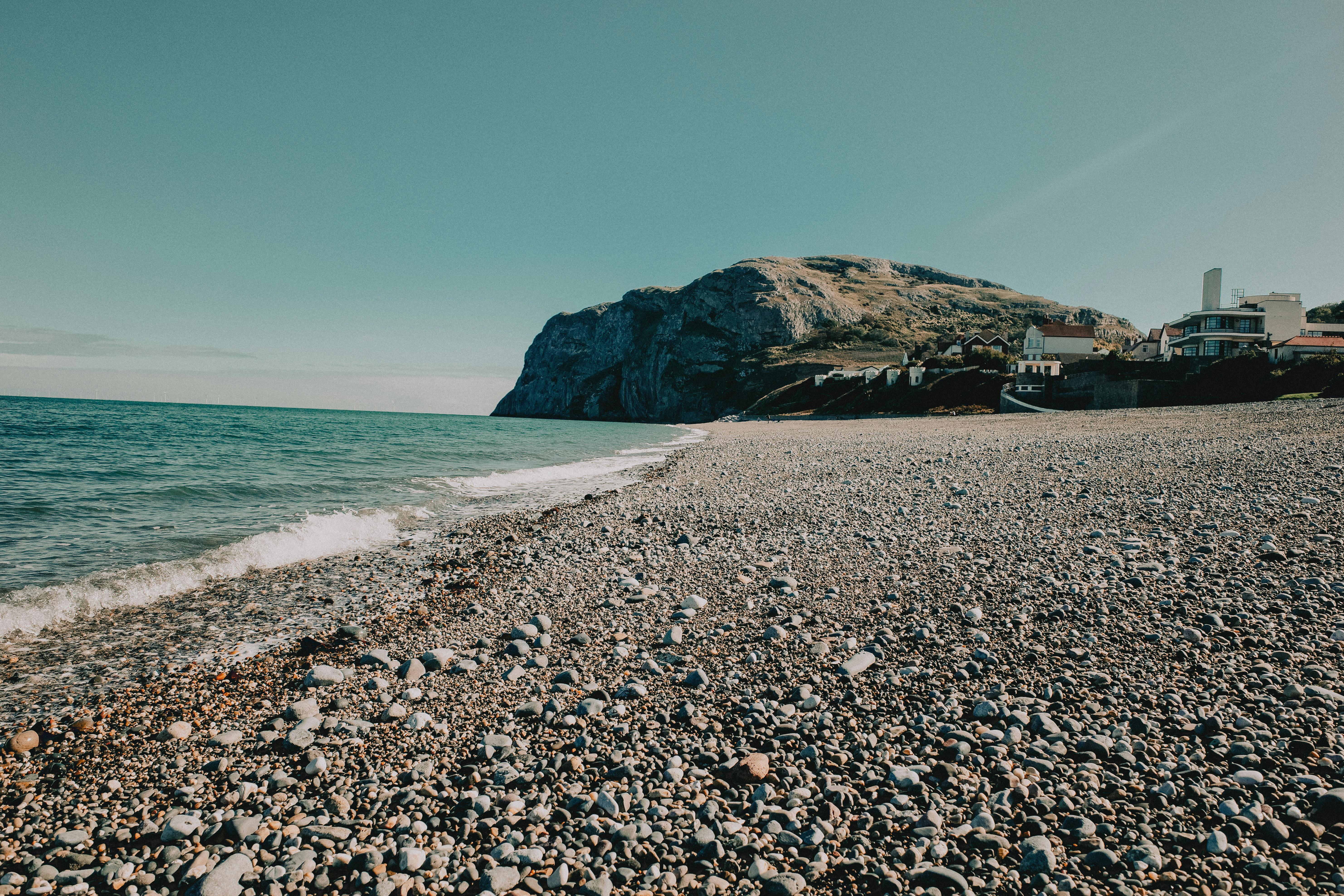 Serene pebble beach at Llandudno, Wales, showcasing coastal waters and rocky mountainside.