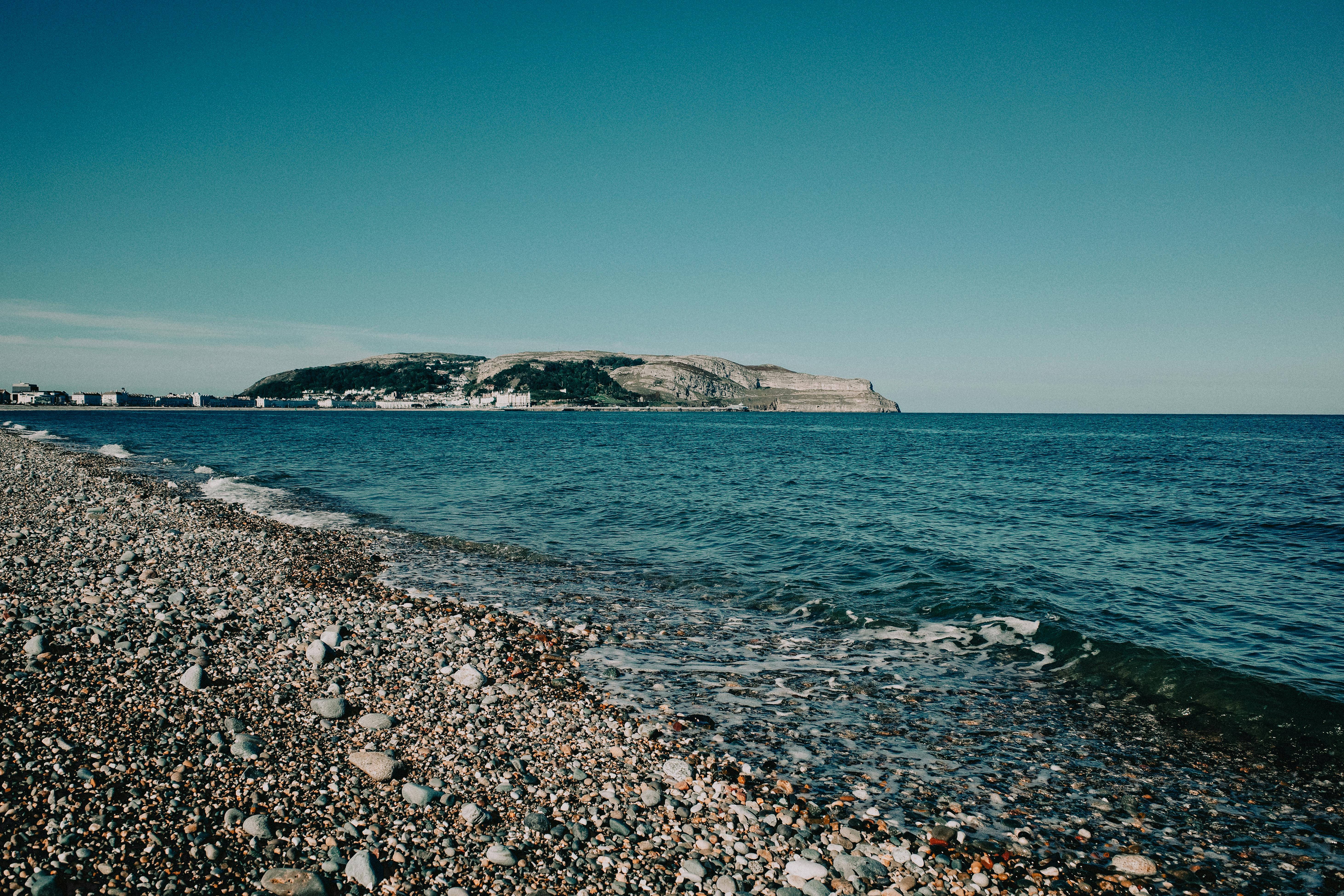 Scenic view of a pebble beach and Great Orme in Llandudno, Wales, under clear skies.