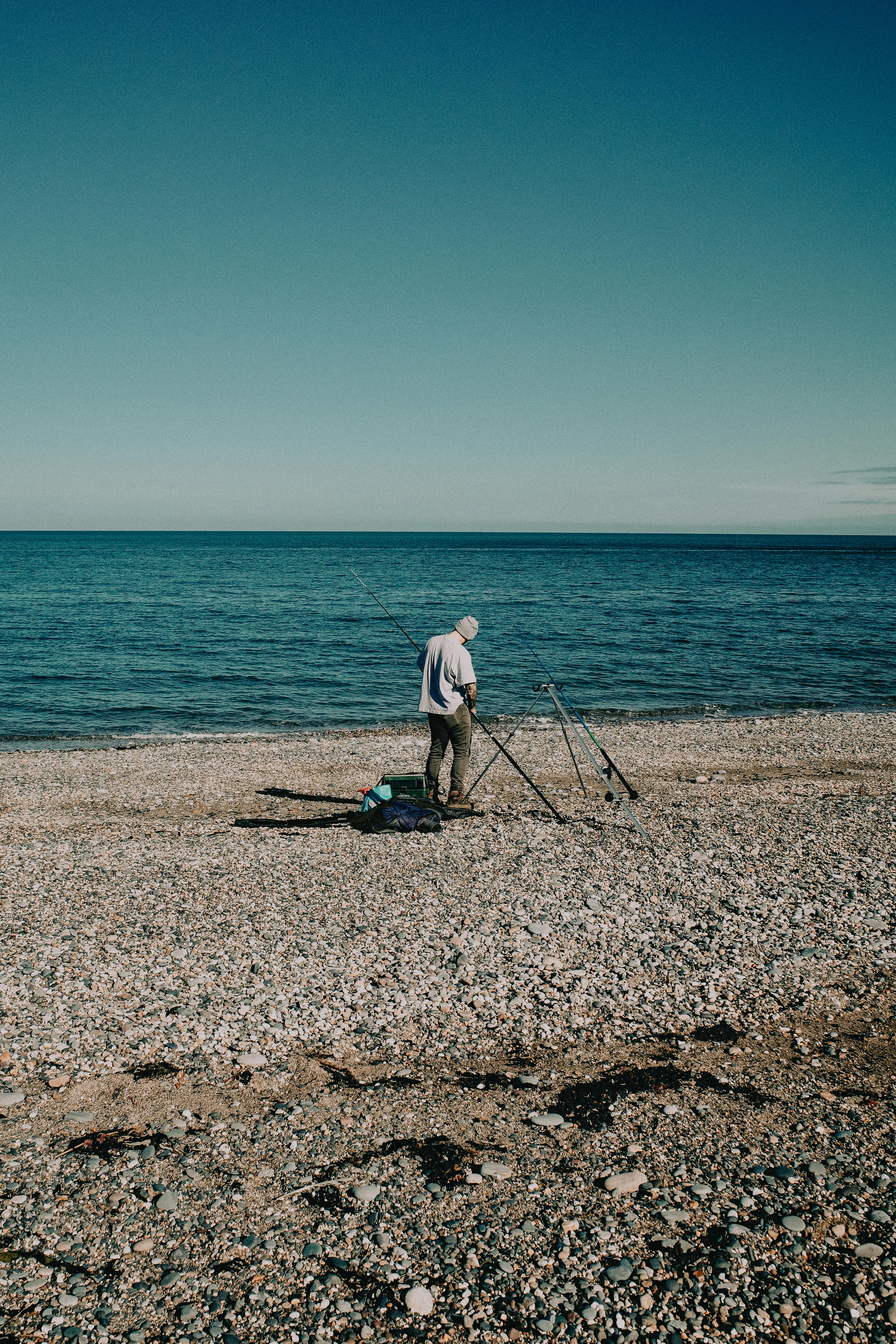 Serene scene of a man fishing on a pebble beach in Llandudno, Wales during a sunny day.