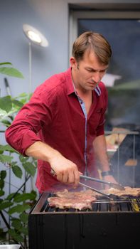 Man grilling meat outdoors in Switzerland, enjoying a summer barbecue party.