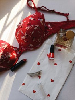Flat lay of red floral lingerie with perfume, lipstick, and nail polish.