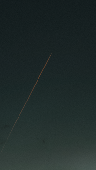 A dark night sky featuring a long, red streak of a meteor moving diagonally.