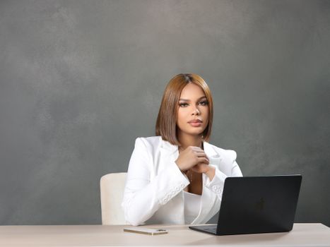 Professional woman in white office attire using a laptop at her desk, exuding confidence and focus.
