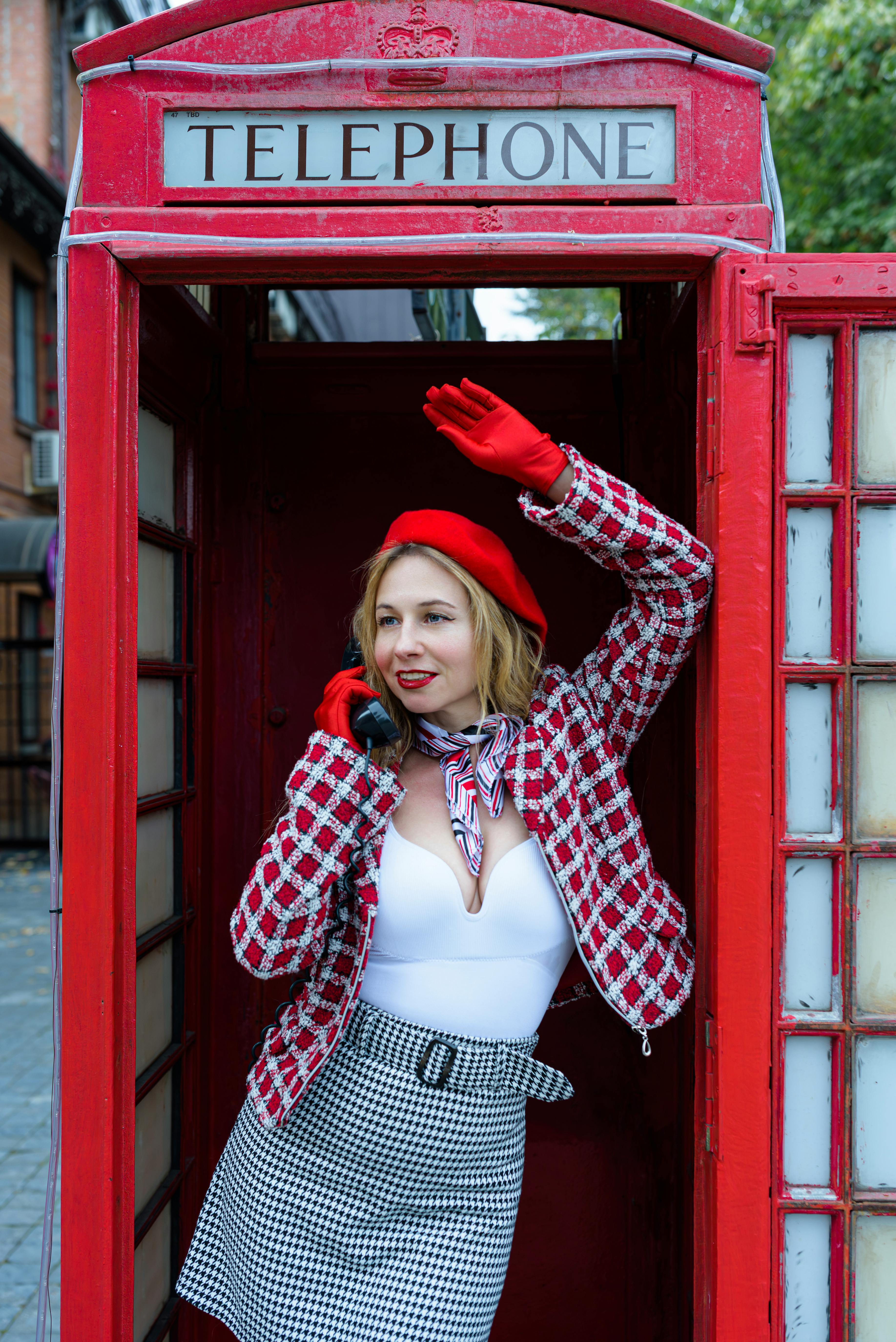 grátis Mulher moderna com roupa vermelha posando dentro de uma cabine telefônica tradicional britânica ao ar livre. Foto profissional