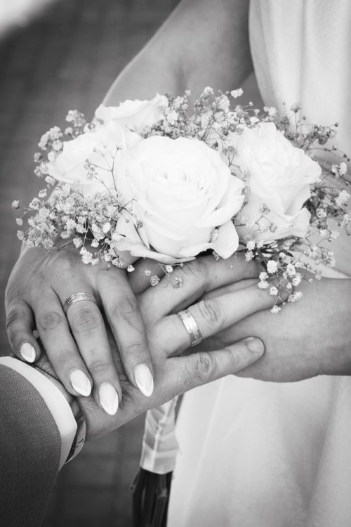 Free Close-up of a couple's hands with wedding rings and a floral bouquet, symbolizing love and commitment. Stock Photo