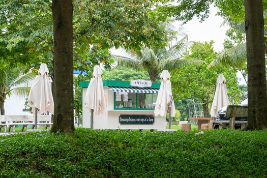 Charming outdoor coffee kiosk surrounded by lush greenery and trees in a peaceful park setting.