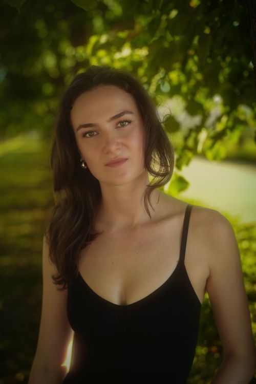 Free A serene outdoor portrait of a woman in a black dress under lush green trees, conveying a peaceful and natural vibe. Stock Photo