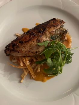 Delicious grilled chicken breast with arugula and crispy fries on a white plate served with sauce.