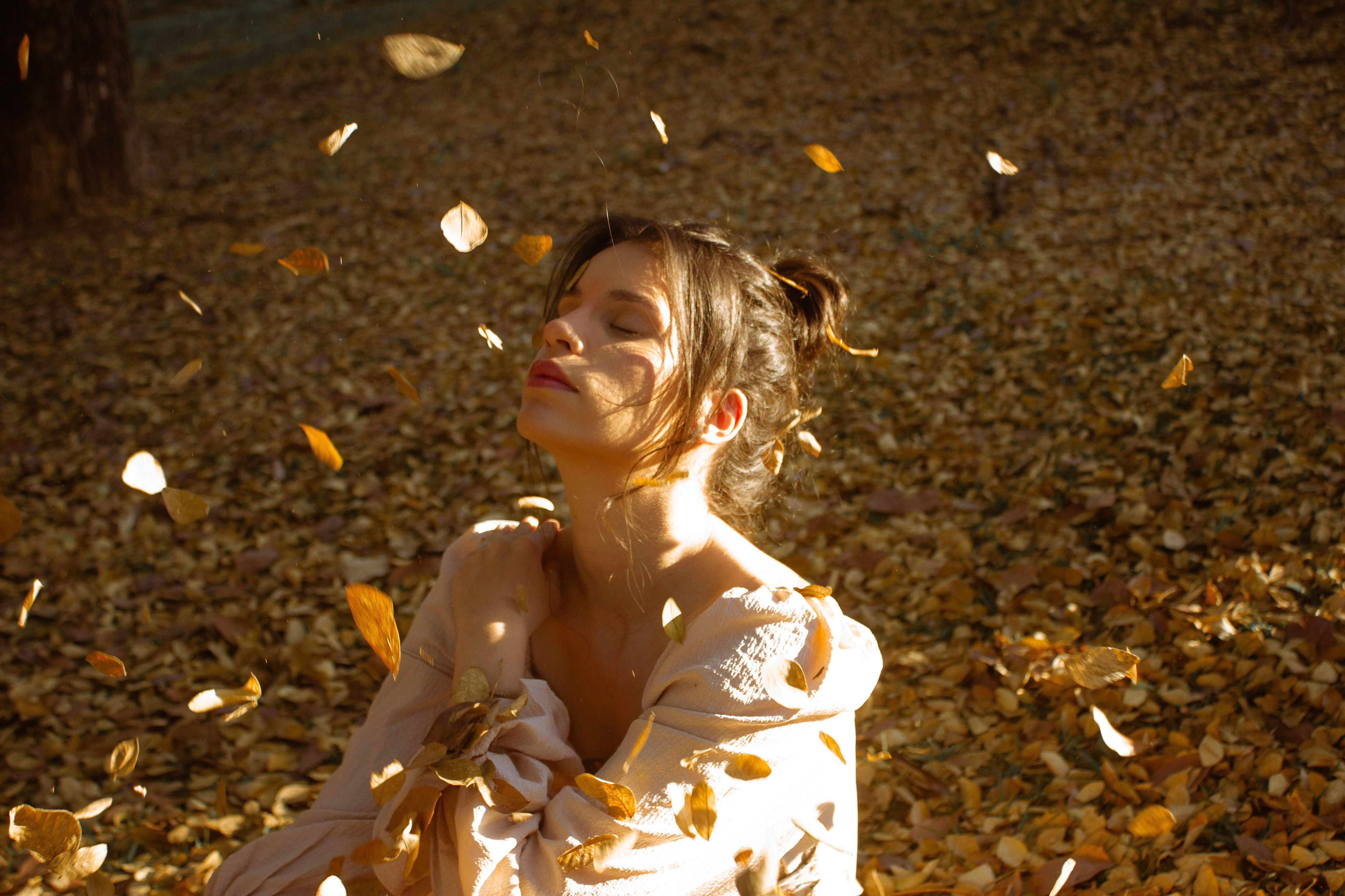 Woman Embraces Fall Leaves in Sunlit Forest · Free Stock Photo