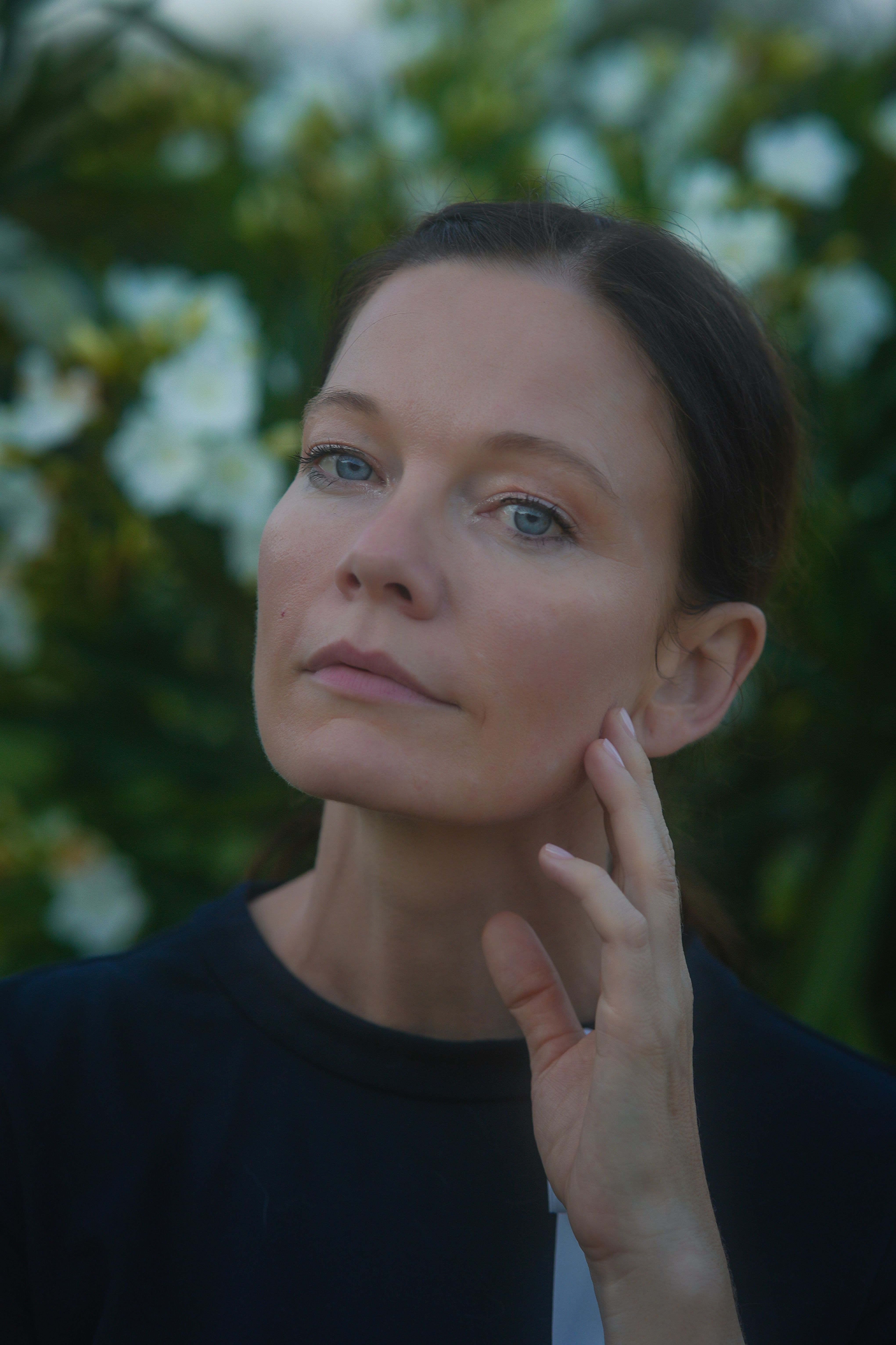 Elegant portrait of a woman amidst green foliage, offering a serene and introspective mood.