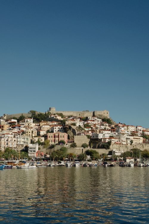 Free Scenic view of a Mediterranean coastal town with a hilltop fortress and vibrant architecture. Stock Photo