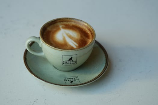A beautifully crafted latte art coffee in a Cafe Kangoo mug on a white marble table.