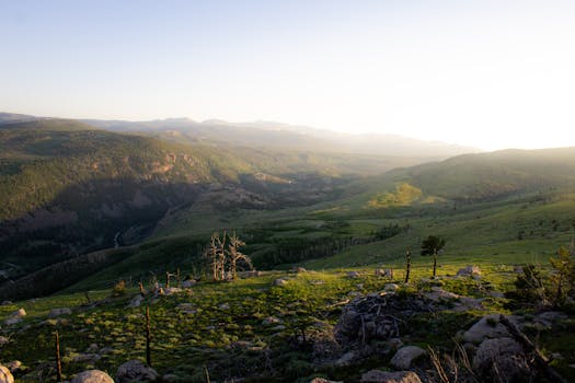Picturesque mountain landscape during sunrise in Wyoming with rolling hills and lush greenery.