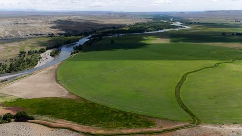 Free Panoramic aerial shot of lush green farmland with irrigation circle and nearby winding river. Stock Photo