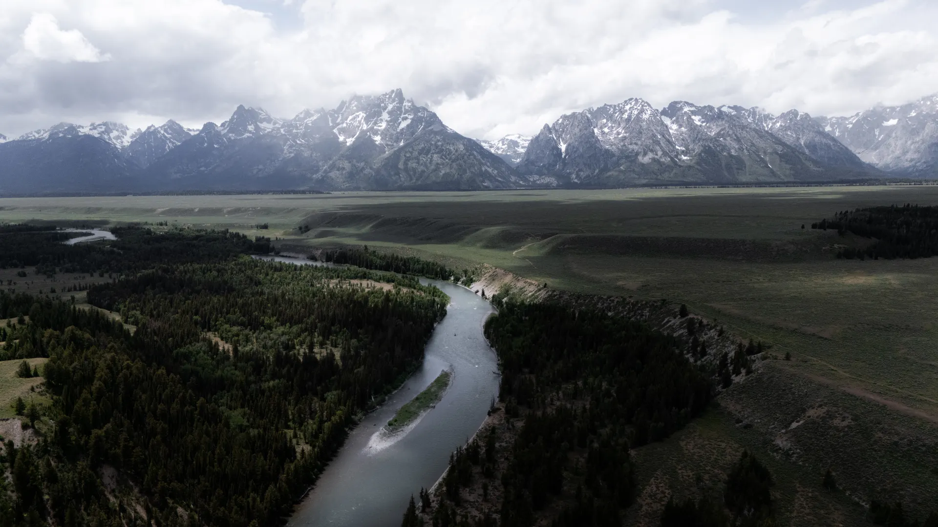 Aerial view of Snake River winding through the lush landscape with the Grand Teton Mountains shrouded in clouds. Aerial view of Snake River winding through the lush landscape with the Grand Teton Mountains shrouded in clouds.
