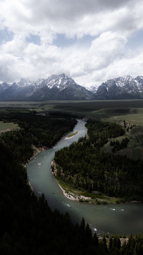 Free Scenic aerial view of Snake River winding through forest with grand Teton mountains in the background. Stock Photo