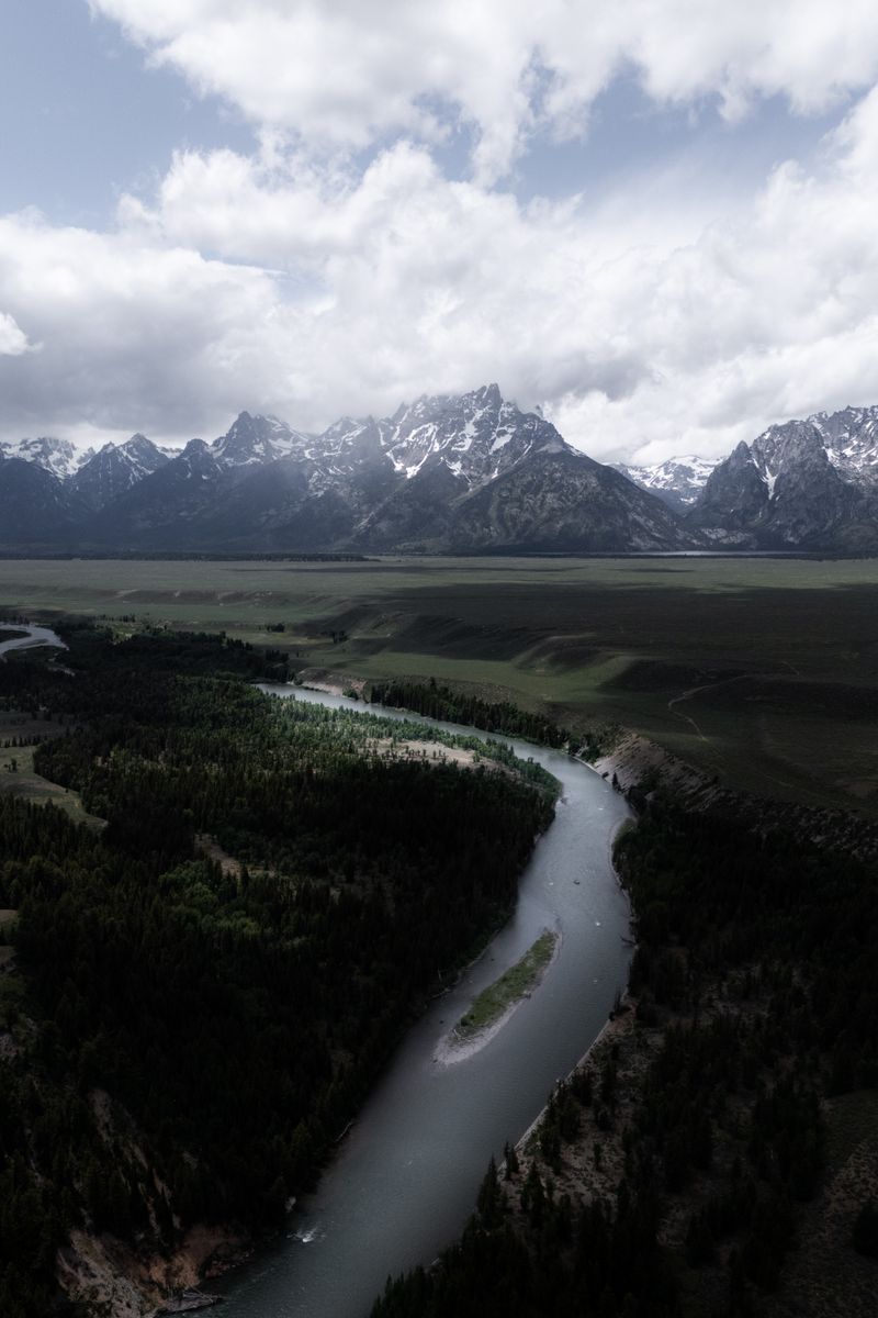 Aerial view of Snake River winding through a valley with the majestic Grand Teton Mountains in the background.