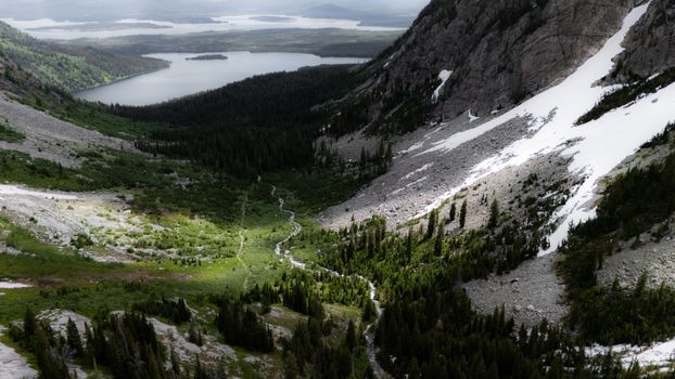 A scenic view of a lush green valley surrounded by rocky mountains with a distant lake. Perfect for nature themes.