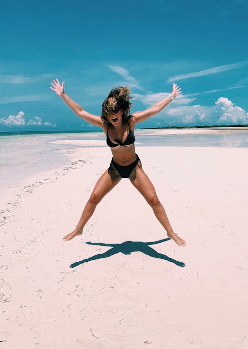 日中のビーチで笑顔と空中でジャンプする女性