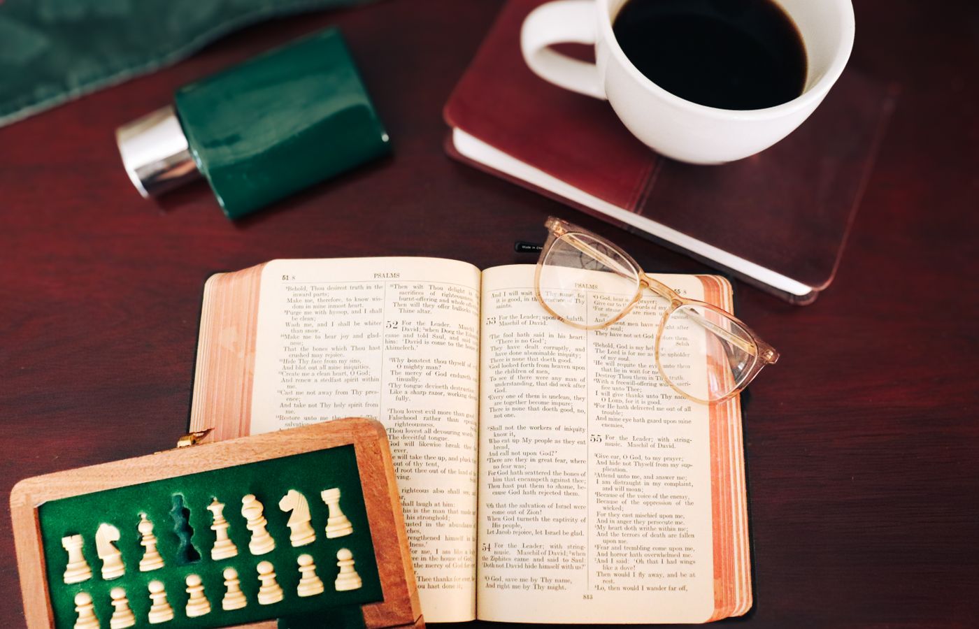 A warm, inviting tabletop scene with an open book, coffee, perfume, and chess pieces.