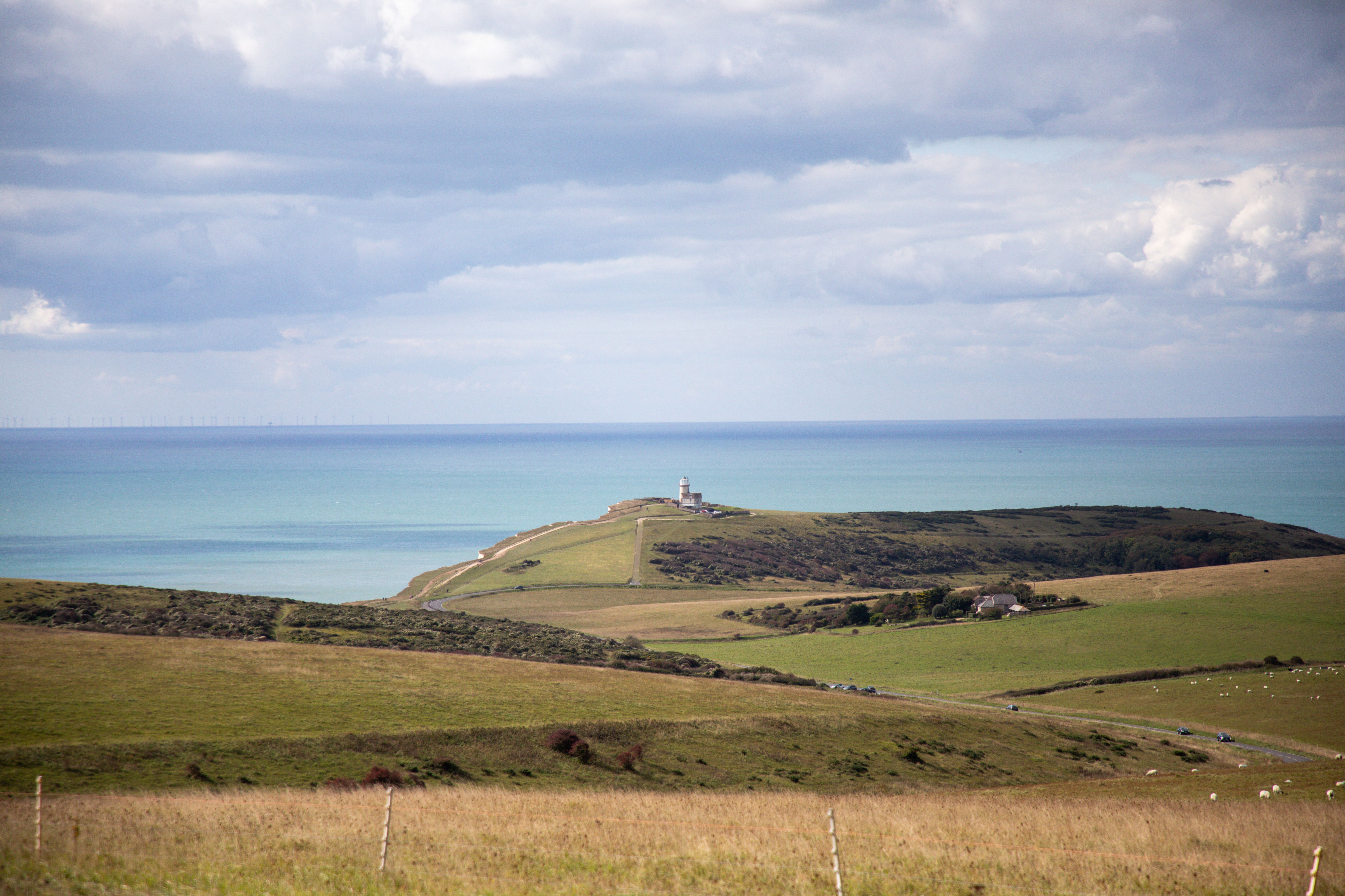 Serene view of the English coastline featuring a distant lighthouse and expansive ocean under cloudy skies.