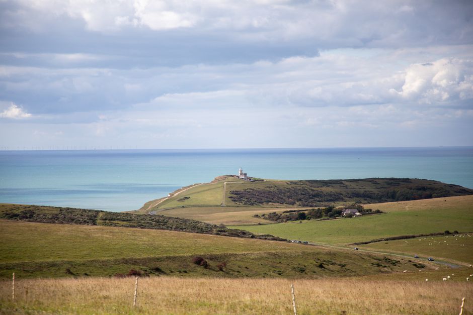 Serene view of the English coastline featuring a distant lighthouse and expansive ocean under cloudy skies.