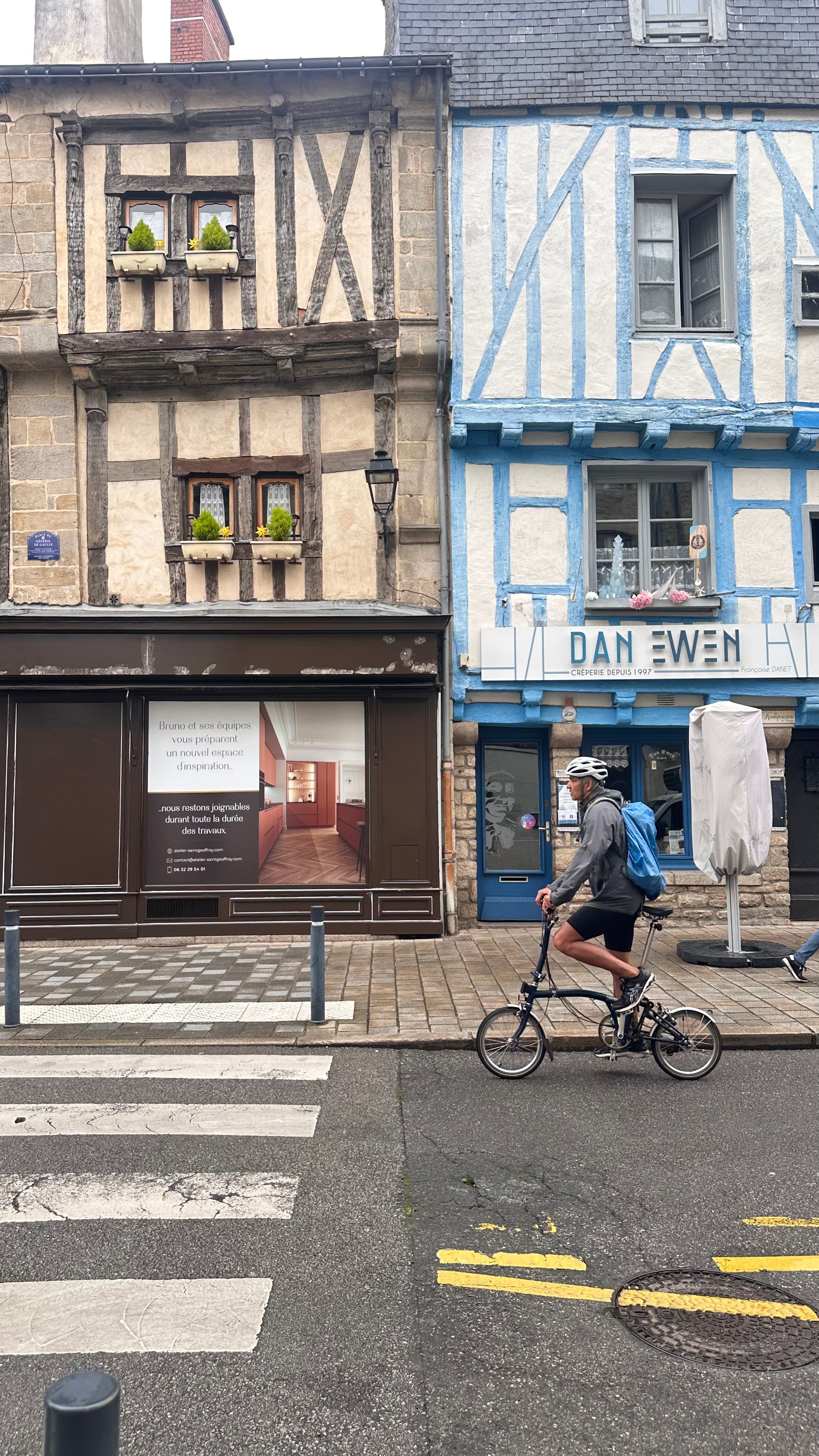 A cyclist rides past colorful half-timbered houses on a street in a charming French town.