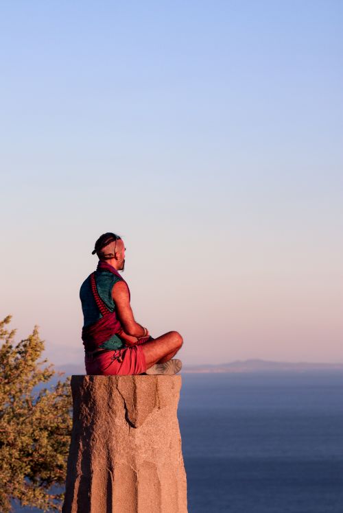 Free Person meditating on pillar overlooking sea in Assos, Türkiye. Tranquil sunset scene. Stock Photo