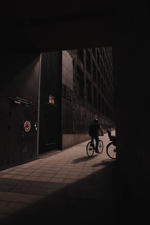 Free Silhouette of a cyclist navigating a dark city alley, creating dramatic shadows. Stock Photo