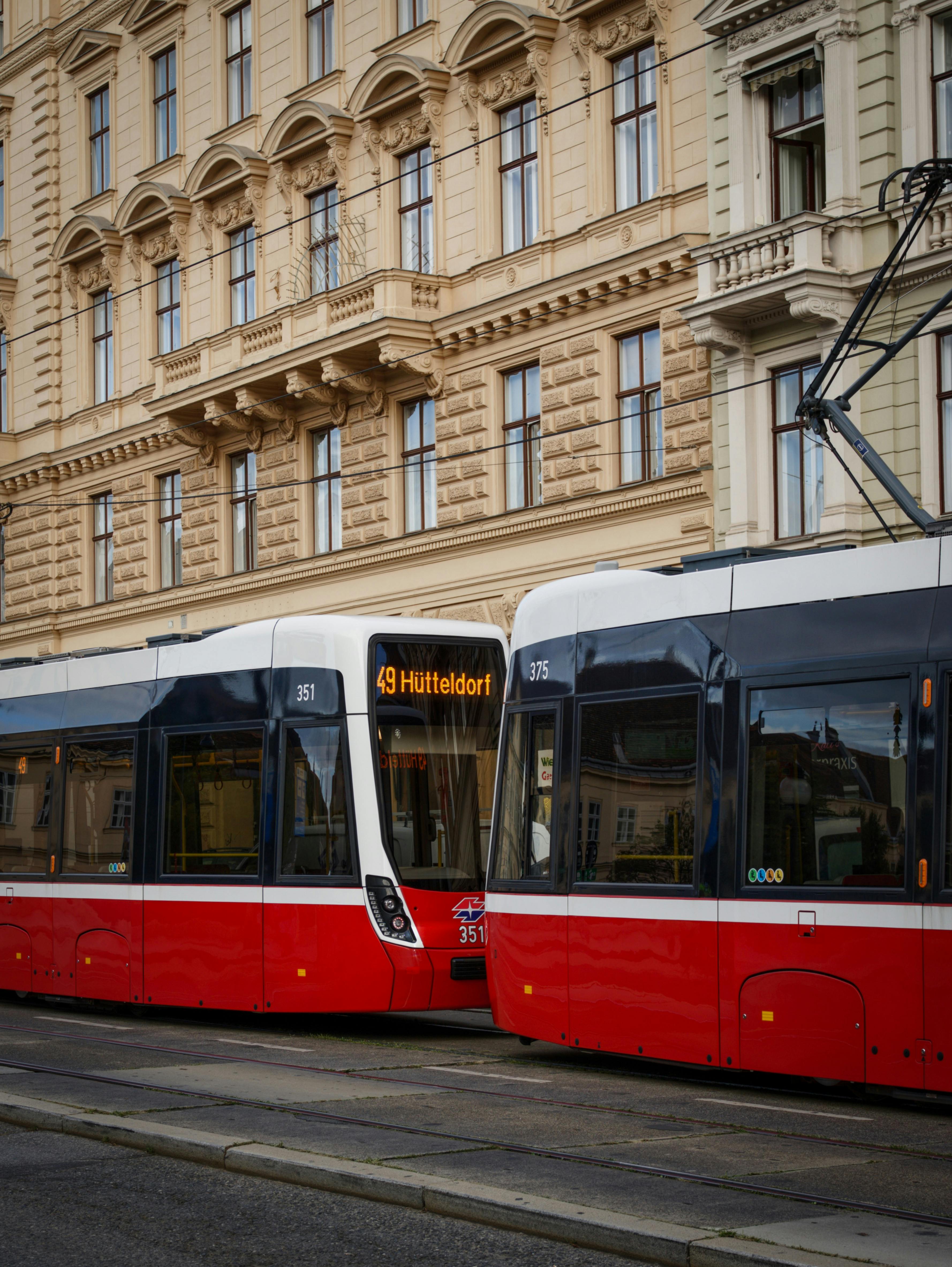 Red and white trams passing by historic architecture in Vienna, Austria. Urban transportation scene.