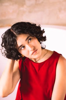 Elegant woman with curly hair in a red dress posing thoughtfully indoors.