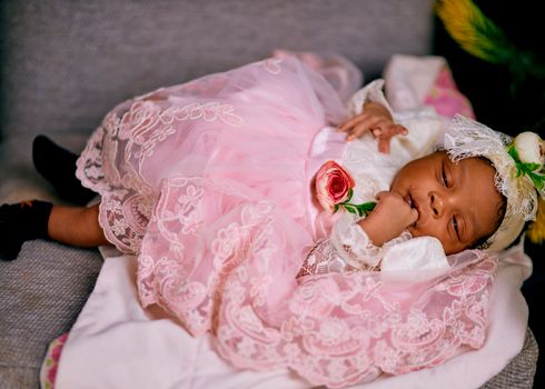 Cute baby in a pink lace dress resting on a sofa, exuding a serene and peaceful vibe.