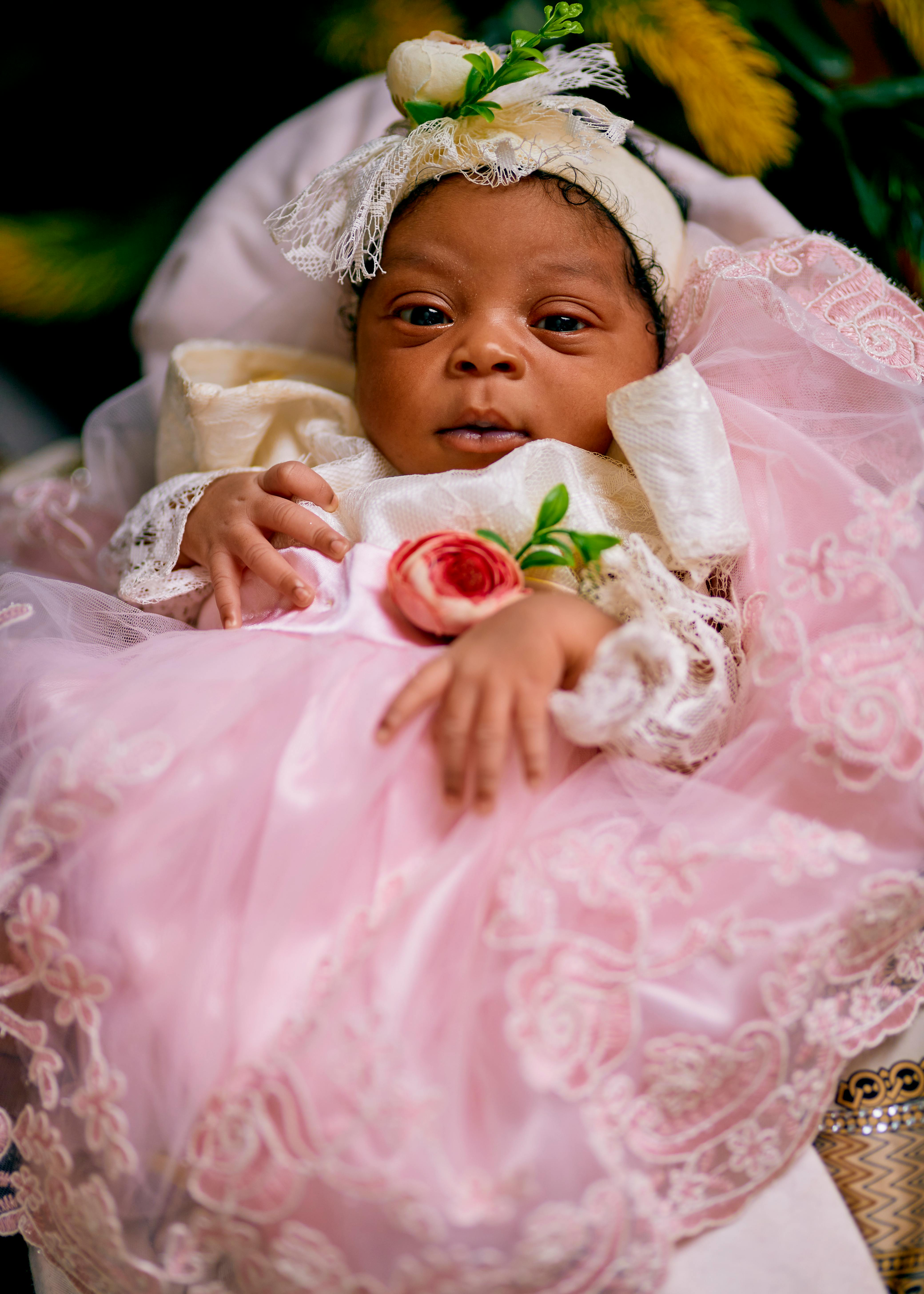 A charming baby dressed in a pink lace dress adorned with roses, showcasing elegance and innocence.