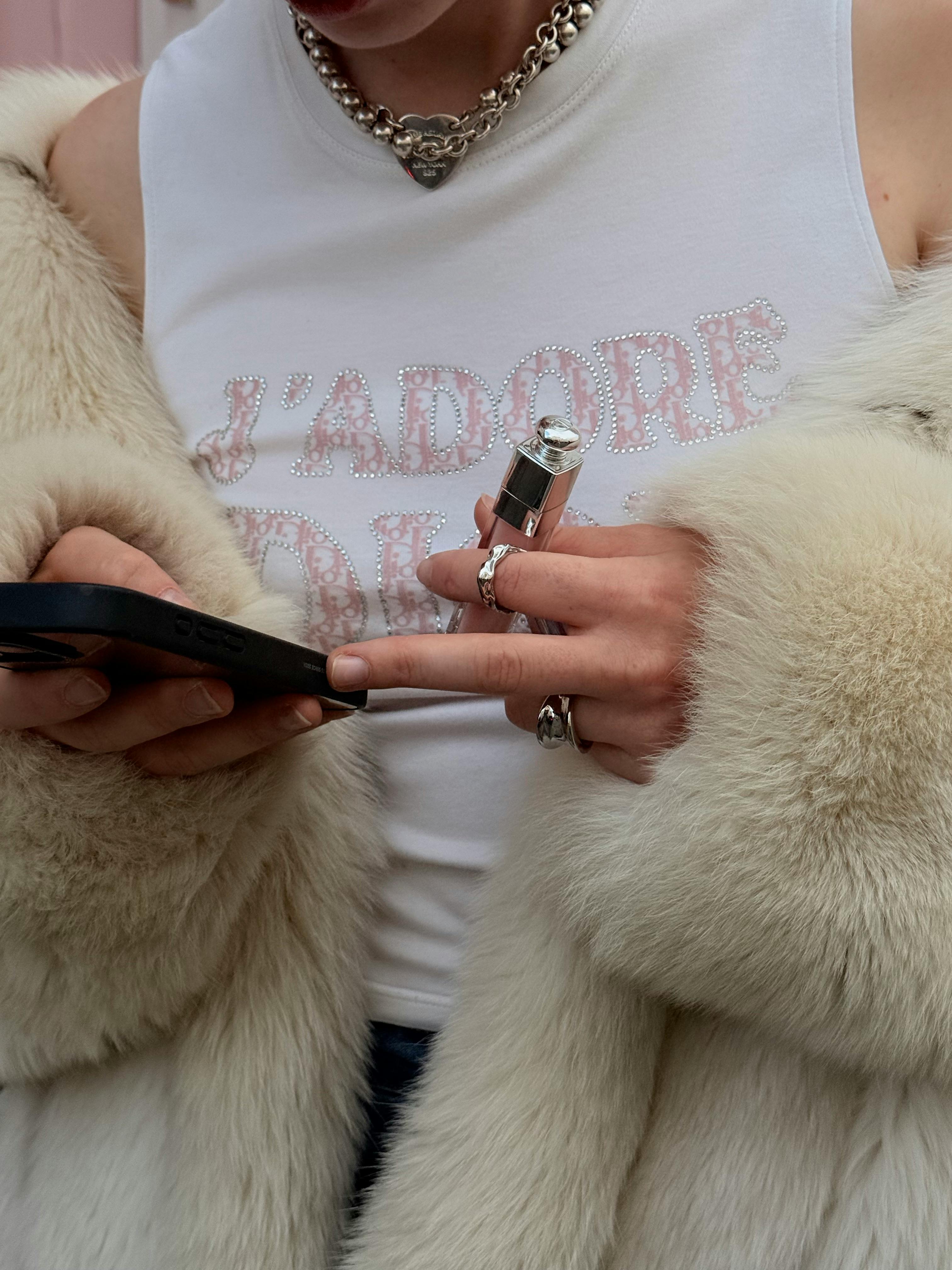 Chic style holding perfume bottle and phone in fur coat and jewelry.