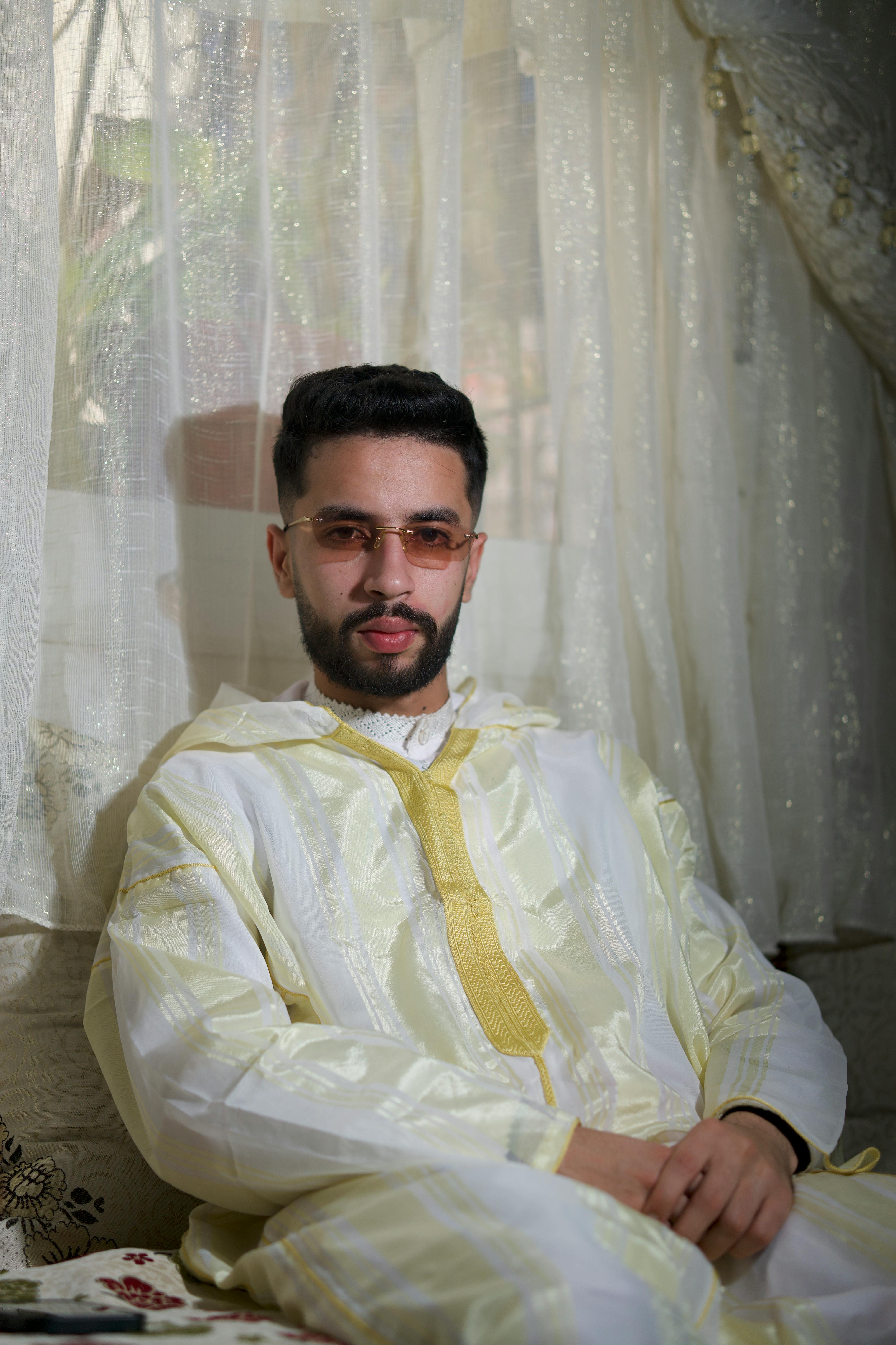 Man in traditional Moroccan attire seated indoors, exuding style and confidence.
