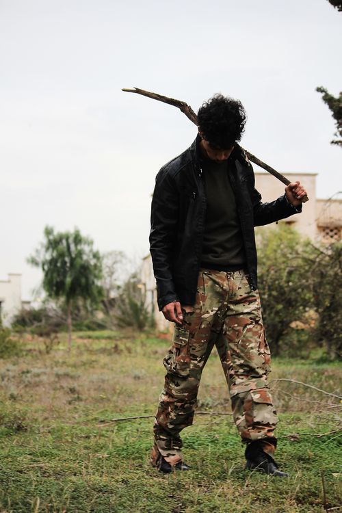 Free A man in a dark jacket and camouflage pants holding a stick in an outdoor setting. Stock Photo
