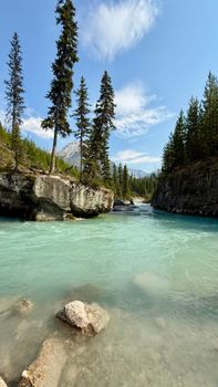 Tranquil river flowing through forested mountains under a clear blue sky.