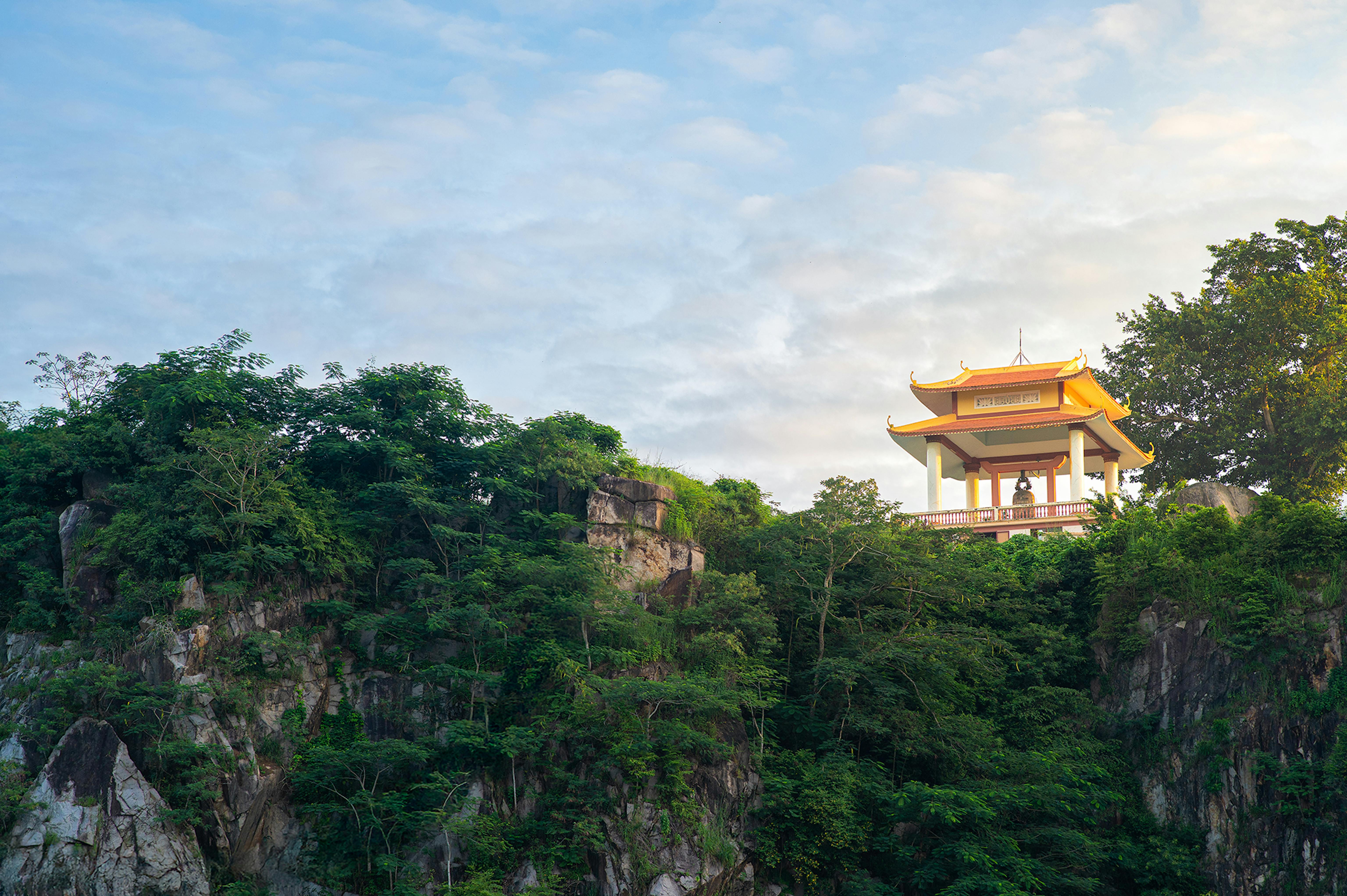 Scenic view of a Buddhist pagoda perched on a cliff surrounded by lush greenery in An Giang, Vietnam.