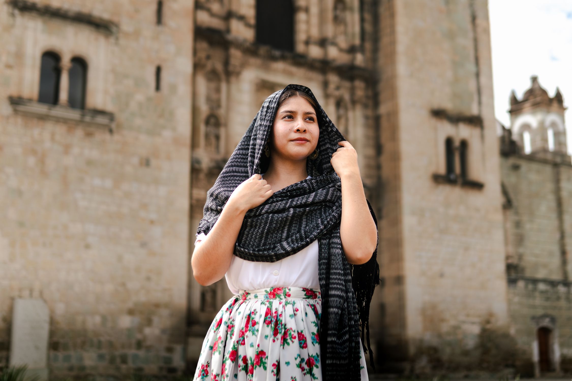 Portrait of a woman in traditional attire in front of a historic building in Oaxaca, Mexico.