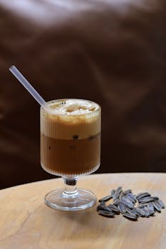 A refreshing iced coffee served in a glass with straw alongside sunflower seeds on a wooden table.