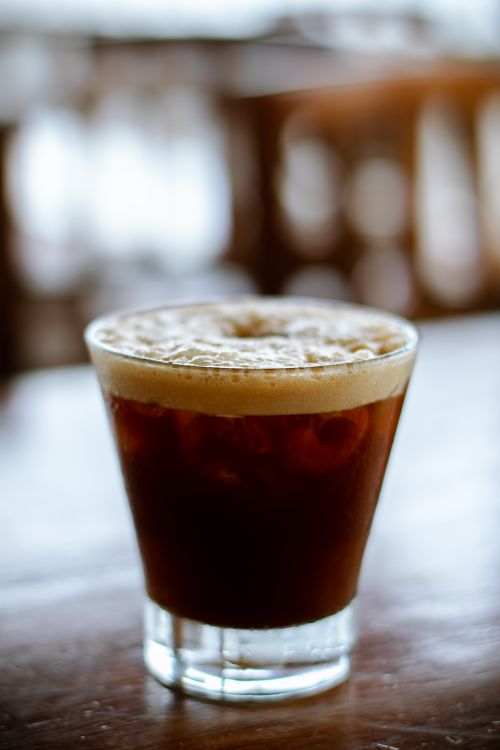 Free Refreshing iced coffee with creamy foam served in a clear glass on a wooden table. Stock Photo
