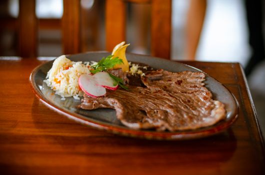 Delicious Mexican grilled beef with rice, radish, and lemon on a plate, served indoors.